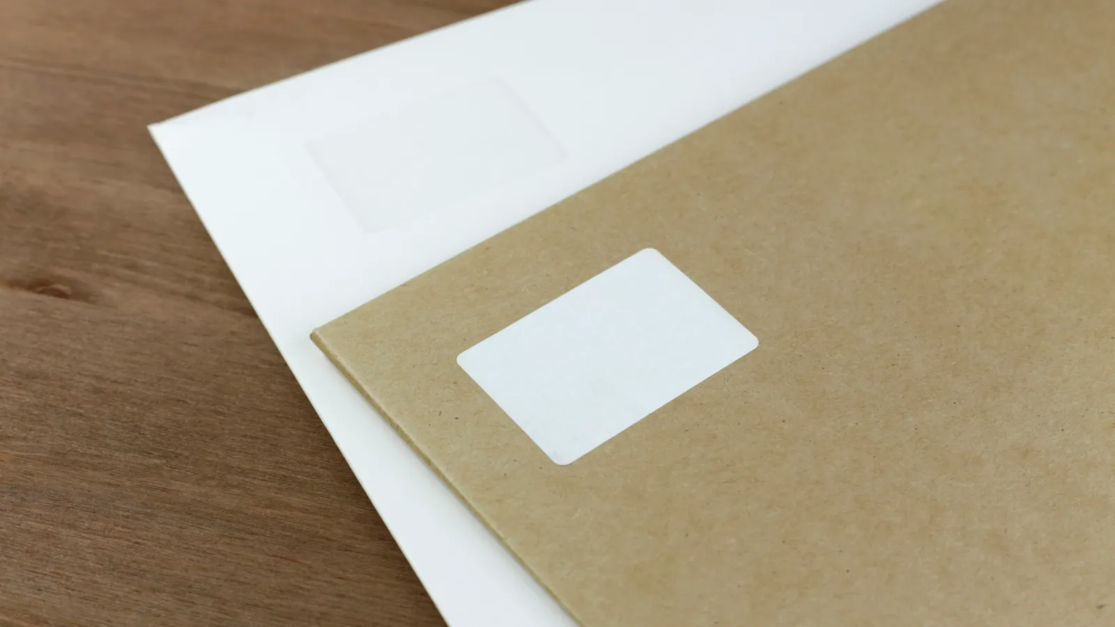 Kraft envelope with a blank address label lying on a white document on a wooden desk