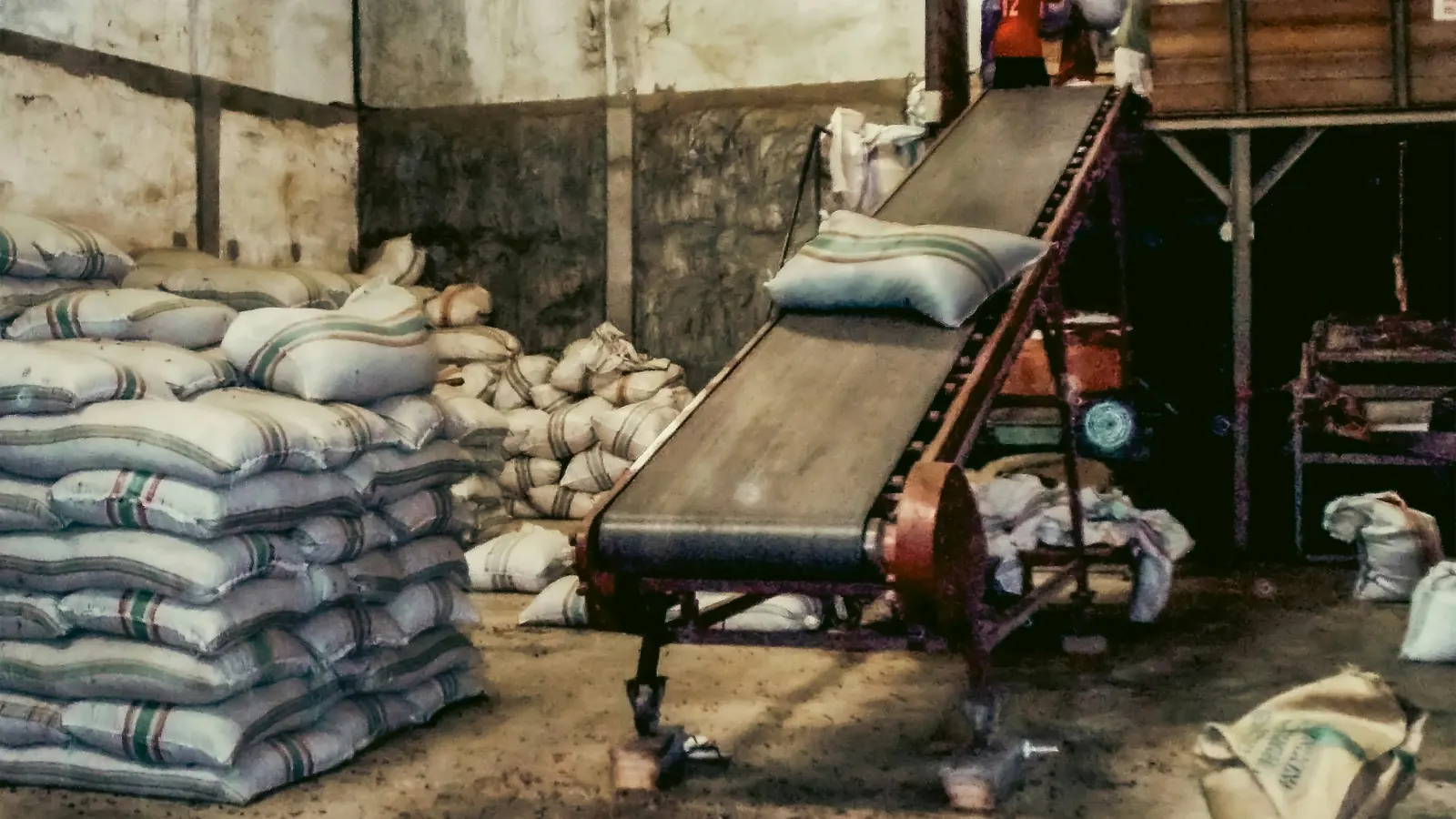 Stacked sacks of bagged cargo beside a conveyor belt in a warehouse