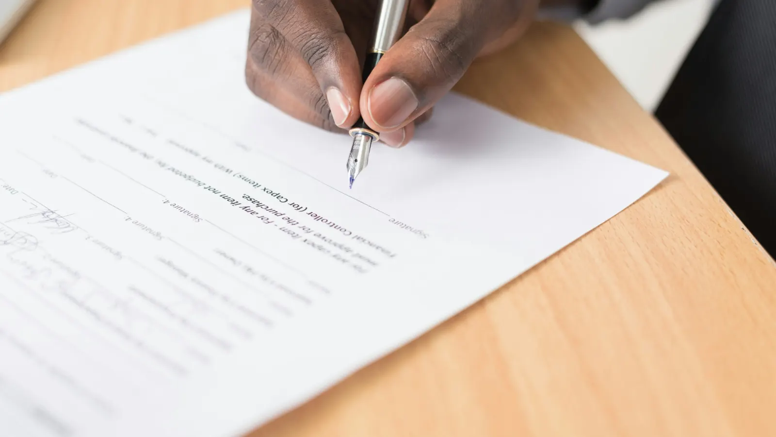 Hand signing a printed approval form with a fountain pen on a wooden desk