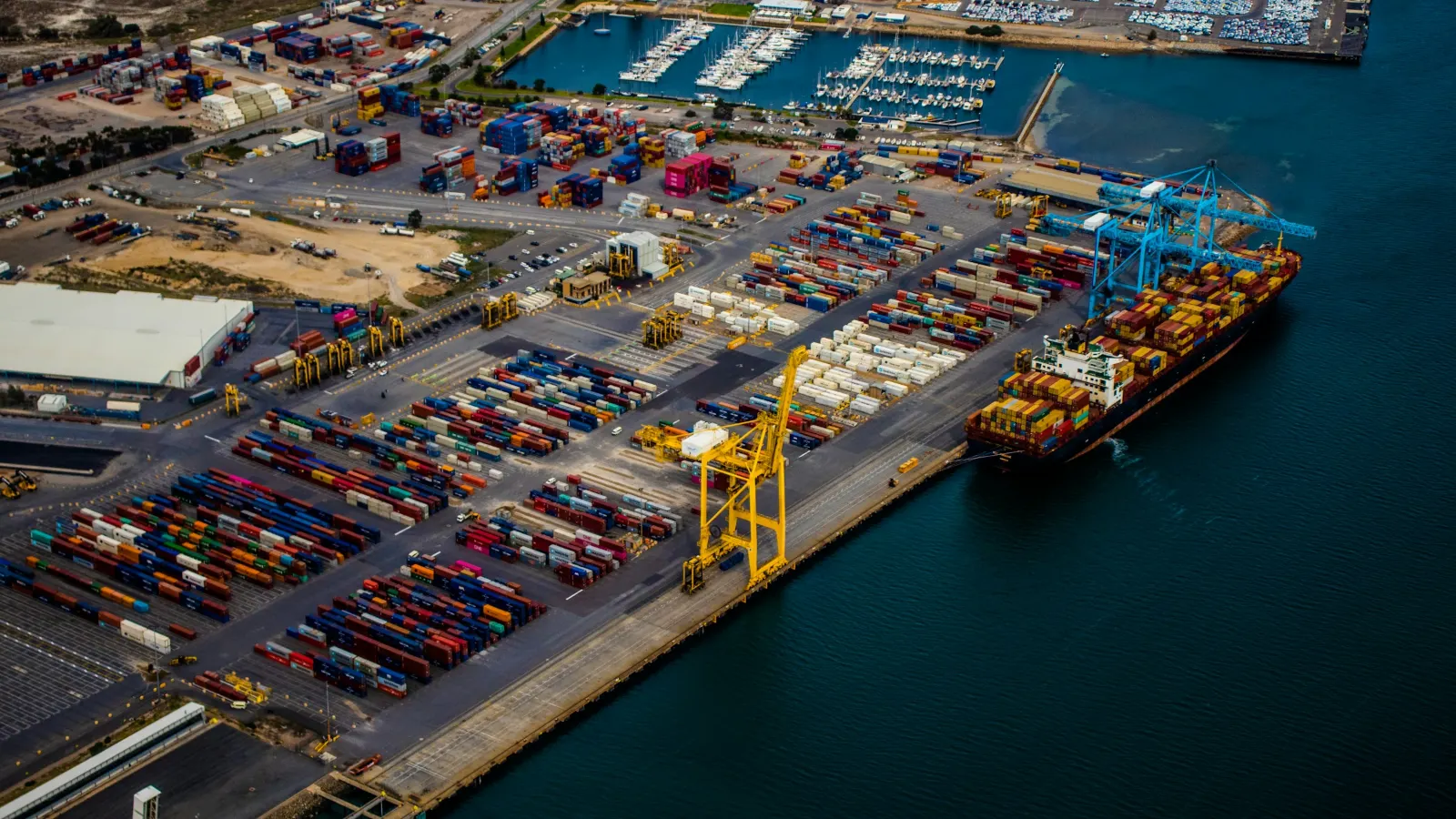 Aerial view of a container terminal with a loaded container ship alongside blue ship-to-shore cranes
